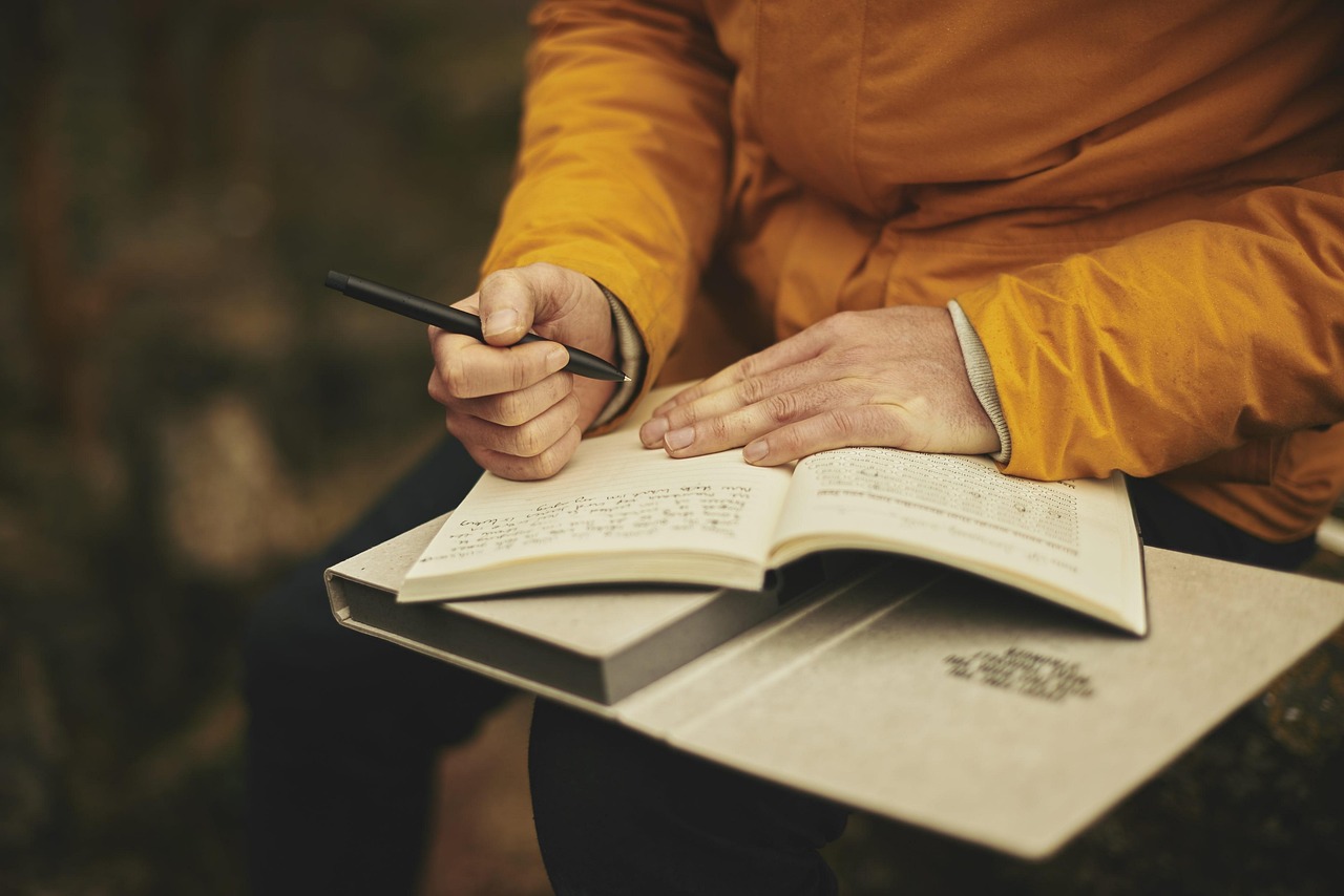 A person outdoors writes in their notebook